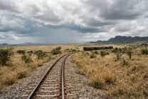 Via férrea atravessando paisagem africana com composição de carga ao fundo