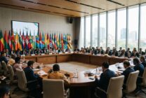 Sala de conferência internacional com delegados reunidos em torno de mesa de negociações